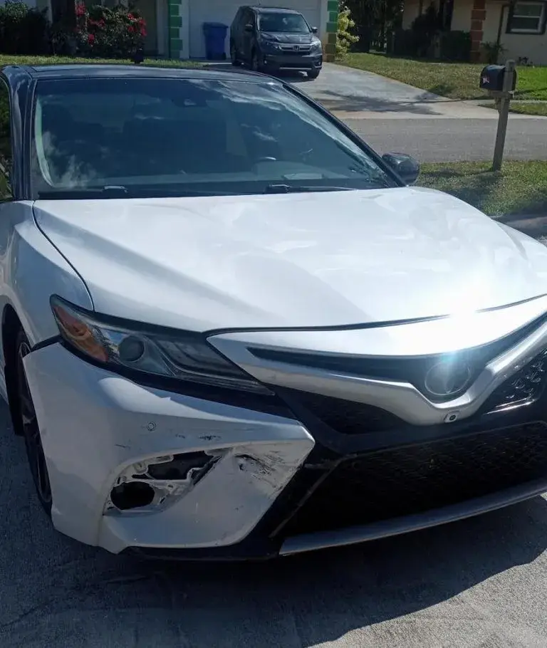 White Toyota Camry with front-end damage before repair